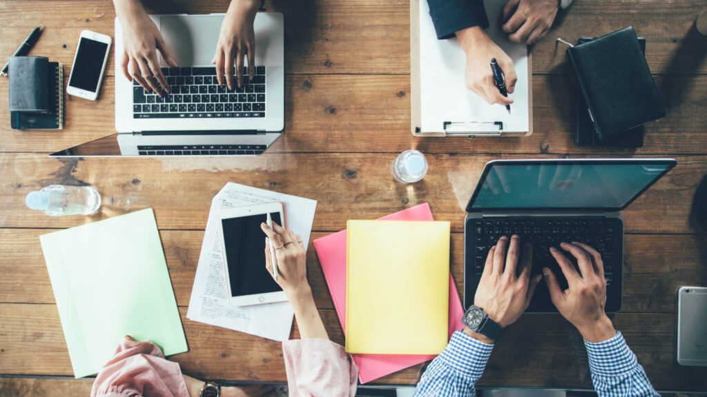 机の上にちらばったパソコンやノートに人の手